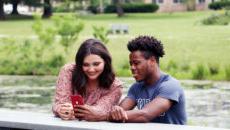 Students on a bench at the lake looking at a phone